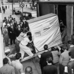 Bild från 1956: två män skjuter en hårddisk på fem megabyte uppför en ramp. Den ser ut att vara 1,80 meter hög och väger enligt uppgift 250 kg.