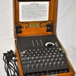 En Enigmamaskin. En trälåda med uppfällt lock. Inuti lådan ser man ett tangentbord. 
